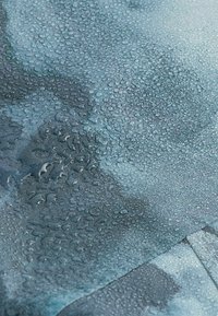 Gros plan sur un tissu bleu imperméable avec des gouttelettes d'eau perlées à la surface, mettant en valeur sa texture déperlante.