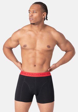 Schwarze Baumwoll-Boxershorts mit elastischem roten Bund, der das Logo "MUCHACHOMALO" trägt. Das Design umfasst kontrastierende Nähte und eine enganliegende Form.