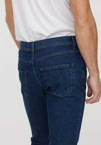 Jeans en denim bleu à coupe ajustée, dotés de deux poches arrière, de détails de couture subtils et d'une ceinture avec passants.