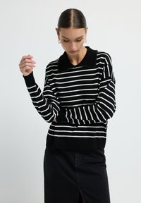 Maglione a righe bianche e nere con colletto nero solido decorato con perline, realizzato in morbido materiale a maglia, abbinato a una gonna nera.