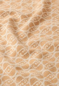 Tessuto con un motivo crema e arancione chiaro, caratterizzato da forme intrecciate e una superficie testurizzata, con dettagli di tessitura visibili.