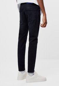 Svarta denimjeans med smal passform, synliga bakfickor och en lätt blekning. Bärs med vita sneakers och grå strumpor.