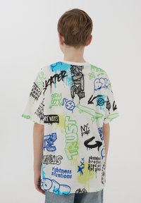 T-shirt a maniche corte di colore bianco con grafiche in stile graffiti colorate. Presenta testi audaci, schizzi e spruzzi di accenti blu e verdi.