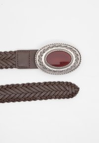 Ceinture en cuir tressé marron avec une boucle ovale en métal ornée d'une pierre rouge au centre, entourée de détails décoratifs en argent.