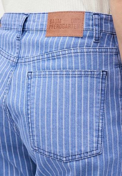 Κοντινό πλάνο πίσω τσέπης τζιν με μπλέ ριγέ μοτίβο και καφέ δερμάτινη ετικέτα που γράφει "Baum und Pferdgarten".