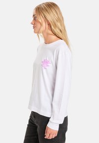 Weißes Langarm-T-Shirt mit einem pinken Blitz-Graphic auf der linken Brust. Einfaches Design mit Rundhalsausschnitt und geradem Saum.