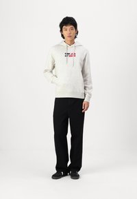 Lys grå hættet sweatshirt med et logo på forsiden, parret med sorte vide bukser og sorte sko. Glat tekstur, afslappet pasform.