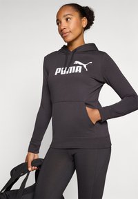 Felpa nera con cappuccio realizzata in tessuto morbido, dotata di tasca frontale, maniche lunghe e logo Puma bianco sul petto.