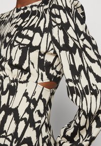 Robe à motifs noir et blanc avec manches longues, tissu texturé et détail découpé à la taille. Design de motifs abstraits audacieux.