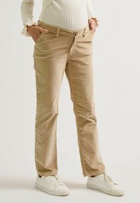 Beige Cordhosen mit gerade geschnittenem Bein und Fronttaschen, ausgestattet mit Reißverschluss und Knopfverschluss, kombiniert mit weißen Sneakern.