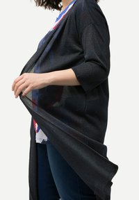 Černý cardigan s otevřeným předním dílem vyrobený z lehkého, lesklého materiálu. Má tříčtvrteční rukávy a splývavý siluetu, která obepíná tělo.