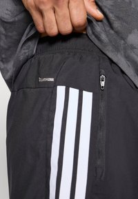 Mustad sportlikud lühikesed püksid lukuga taskuga, Climacooli kaubamärgiga ja kolme valge vertikaalse triibuga külgedel. Kerge materjal.