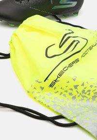 Sac de football Skechers en jaune vif avec une surface texturée, présentant un logo noir et un motif abstrait argenté en bas. Cordons de serrage noirs attachés.