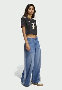 Μαύρο κοντό μπλουζάκι από τζέρσεϊ με κόκκινες λεπτομέρειες και λογότυπο, σε συνδυασμό με φαρδιά τζιν παντελόνια σε μπλε χρώμα με πλαϊνές ρίγες και χαλαρή εφαρμογή.