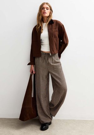 Brown cropped jacket, white fitted top, houndstooth patterned wide-leg trousers, and black platform shoes. Brown tote bag over shoulder.
