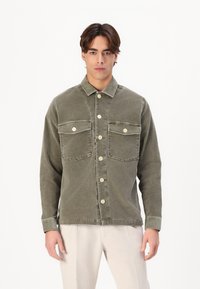Olijfgroene corduroy overhemdjack met twee borstzakken, knopen aan de voorkant en een kraag. Zichtbare stiksels en een ontspannen pasvorm.