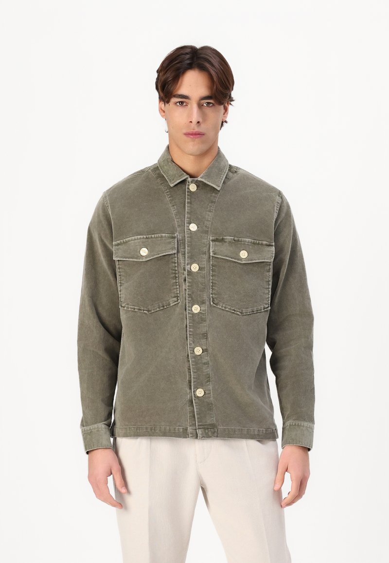 Olijfgroene corduroy overhemdjack met twee borstzakken, knopen aan de voorkant en een kraag. Zichtbare stiksels en een ontspannen pasvorm.