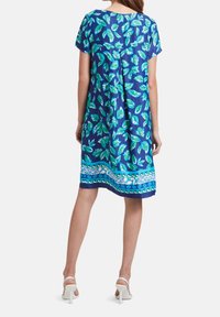 Vestido floral azul con mangas cortas, que presenta patrones de hojas verdes y un dobladillo estampado en azul y blanco. Textura de tela suave.