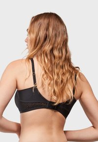 Sujetador negro con detalles de panel de encaje, tirantes ajustables y una textura suave, visto desde atrás con cabello largo y ondulado cayendo.