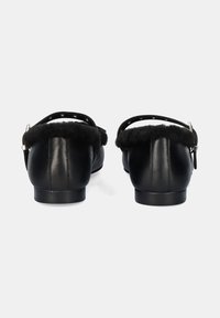 Vista trasera de zapatos de cuero negro con un suave ribete de piel de pelo negro, correa ajustable con herrajes plateados y un tacón bajo y redondeado.
