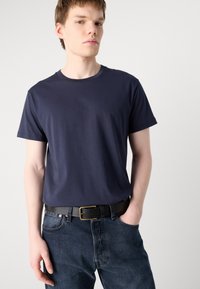 T-shirt en coton bleu marine à manches courtes, coupe décontractée. Assorti à un jean en denim noir et une ceinture en cuir noire avec une boucle en or.