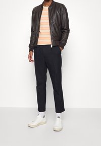 Hnědá kožená bomber bunda, pruhovaný oranžovo-krémový svetr, černé kalhoty a bílé tenisky s krémovými podrážkami. Jednoduchý design, volný střih.