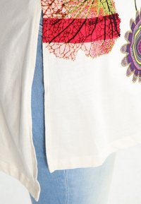 Vit bomulls-T-shirt med färgglad blommönster på framsidan, med sidslits och i kombination med ljusblå denimjeans.