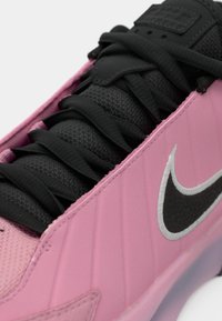 Gros plan d'une basket Nike rose avec des lacets noirs, une languette noire et un logo Nike swoosh noir sur le côté.