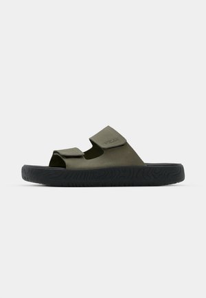 Chanclas de goma verdes con dos correas ajustables y una suela negra texturizada con un patrón de banda. Logo de la marca visible en la correa.