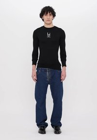 Schwarzes Langarmshirt mit grafischem Logo, kombiniert mit blauen, locker sitzenden Jeans mit Knopfdetails und geradem Bein.