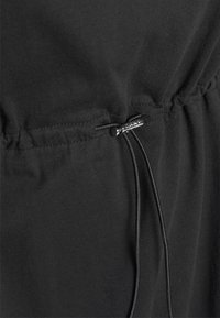 Svart tyg med en samlad design och justerbar dragsko med metallisk detalj, som visar en slät och mjuk textur.