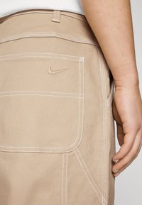 Beige shorts i kraftig tyg med vit sömnad. Har en bakficka med en liten broderad Nike-logotyp.