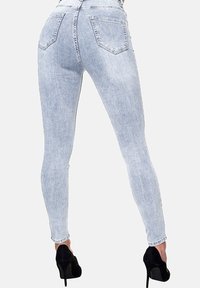 Vaqueros ajustados de tiro alto en azul claro con una textura desgastada, cuatro bolsillos y costuras cosidas, combinados con zapatos de tacón negro.