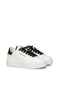 Sneakers bianchi in pelle con lacci neri, un accento sul tallone in pelle nera texturizzata e un logo sul lato. Suola piatta in gomma con una finitura liscia.