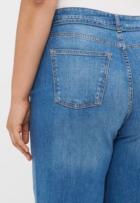 Blue denim jeans feature a classic design with a rear pocket, visible stitching, and a subtle fade. The fabric has a smooth texture.