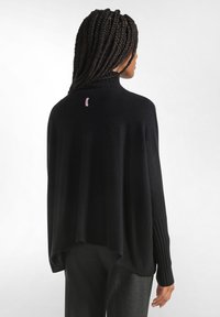 Zwarte pullover trui met een hoge halslijn, geribde mouwen en een losse pasvorm. Kenmerkt zich door een klein roze label aan de achterkant. Zachte textuur.