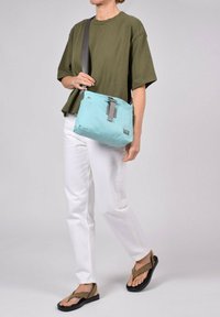 Sac bandoulière bleu clair avec une sangle et une boucle grises ; matériau doux et rembourré ; forme rectangulaire ; minimalisme de la marque sur le devant.