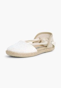 Valge espadrill tekstureeritud kangast ülemise osa, elastse rihmaga ja jootüvega. Omab suletud varbaosa ja pehmeid, neutraalse tooni aktsente.