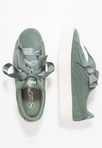 Grüne Wildledersneaker mit Satinschnürsenkeln und einer weißen Gummisohle. Mit einem Logo auf der Zunge und strukturierten Seitendetails.