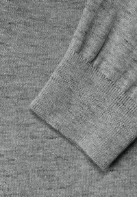 Grått stickat tyg detaljer som visar en mjuk textur, med en muddhem och ribbade kanter för struktur. Subtil färgvariation.