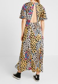 Frau in einem bunten, blumigen Midikleid mit offenem Rücken und luftigen Ärmeln, kombiniert mit schwarzen High-Top-Sneakern.