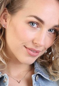 Zilveren V-vormige studoorbellen en een bijpassende V-vormige hangerketting, gedragen met een lichtdenim jack, met subtiele textuur.