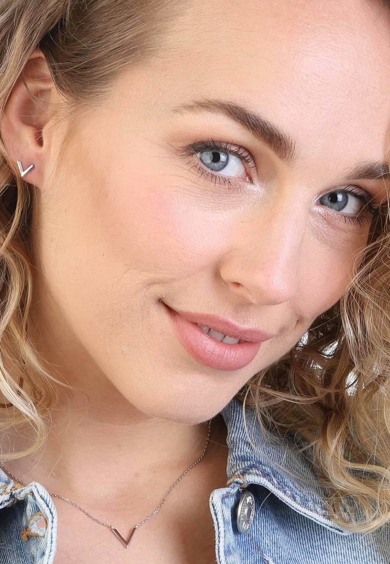 Zilveren V-vormige studoorbellen en een bijpassende V-vormige hangerketting, gedragen met een lichtdenim jack, met subtiele textuur.