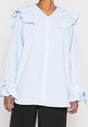 Lichtblauwe en witte verticale gestreepte blouse met grote gerimpelde kraag en gestrikte ruches manchetten, gedragen met een zwarte broek.
