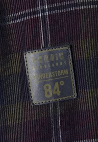 Karierte Textilie in Violett-, Grün- und Blautönen; mit einem aufgenähten schwarzen Etikett mit der Aufschrift "NORDIC WOODLANDS VANDERSTORM 84°."