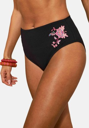 Femeie care poartă slipi de bikini negri cu talie înaltă, texturați, cu broderie florală roz pe lateral și brățări roșii la încheietură.