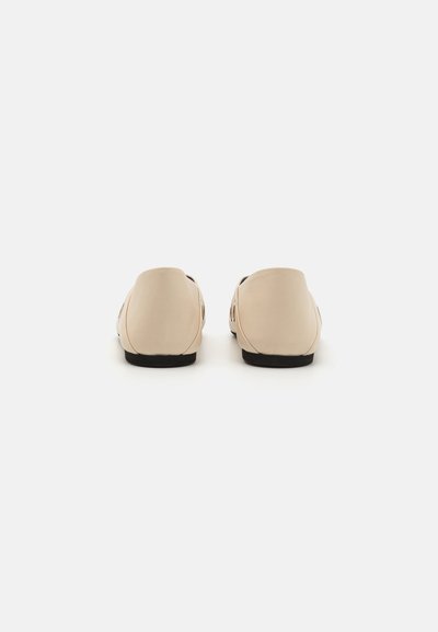Beige slip-on shoes with a smooth, matte finish, rounded back, rubber sole, and cut-out detailing on the sides.