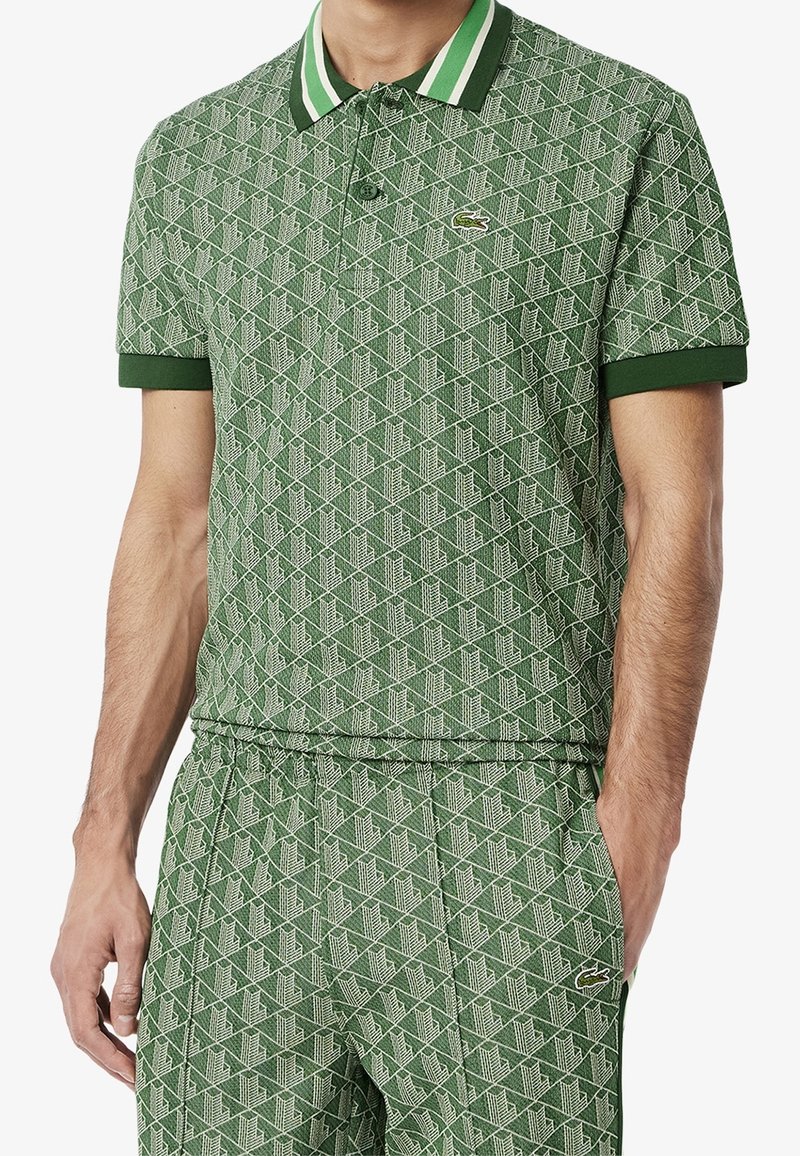 Polo shirt vert à motifs avec un design géométrique blanc, col et poignets côtelés en vert foncé, arborant un petit logo sur la poitrine.