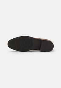 Semelle de chaussure en cuir brun avec une semelle extérieure en caoutchouc noir texturé présentant un motif géométrique et un profil distinct pour l'adhérence et la durabilité.