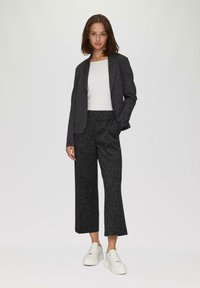 Blazer noir texturé et pantalon large assorti portés avec un haut blanc et des baskets à plateforme blanches. Lignes simples et silhouette contemporaine.